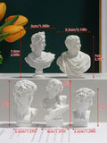 White Greco-Roman bust statues displayed with vases, laptop, papers, and poster.
