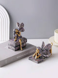 Fairy figurine sitting on stacked books with long hair and detailed wings.