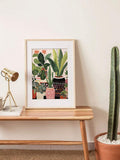 Matted tropical planter artwork beside task lamp and potted cactus