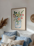 Framed watercolor bouquet in a blue glass jar above layered blue bedding