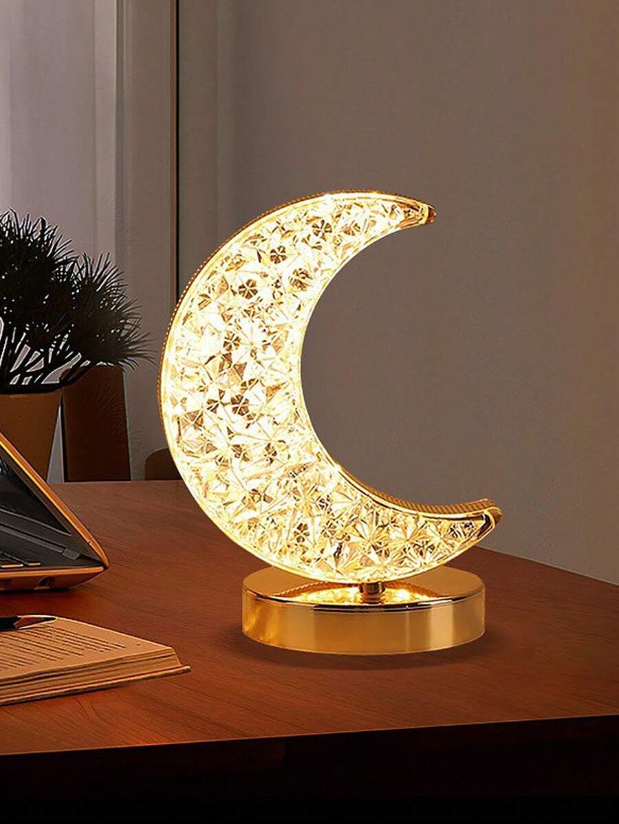 LED crystal crescent moon lamp glowing warm yellow on wooden desk with gold base.