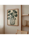Framed dark green flower vase print hanging beside wood shelving and cane chair