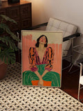 Large framed woman portrait leaning by modern chair and plant