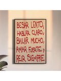 Black framed Spanish quote artwork on a softly lit wall beside large plant leaves