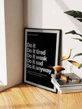 Framed black consistency poster leaning on floor near plant leaves and wooden bird decor