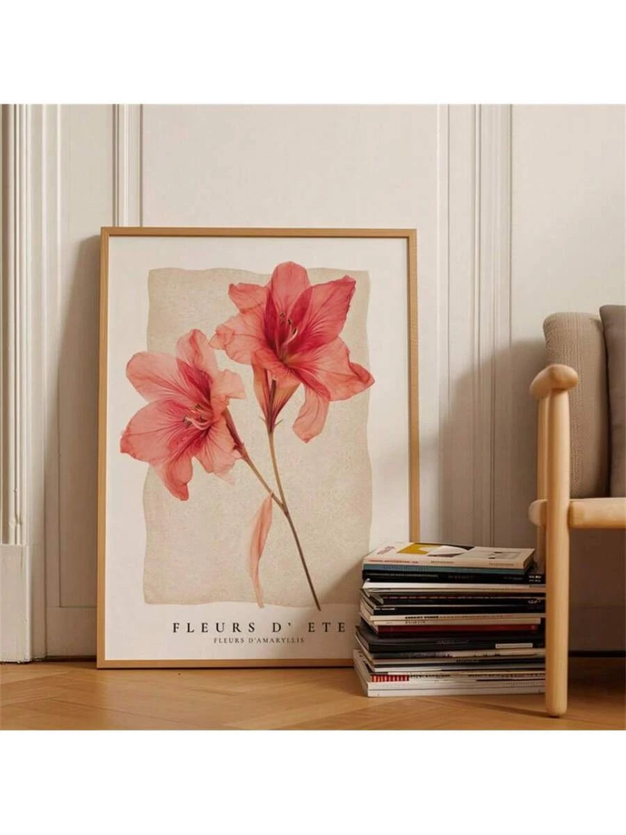Coral amaryllis floral print in a light-wood frame beside stacked books and a chair