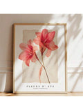Framed coral amaryllis botanical artwork illuminated by sunlight against a neutral wall