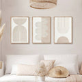 Neutral geometric triptych above a styled bed with pampas grass and a woven wall hat