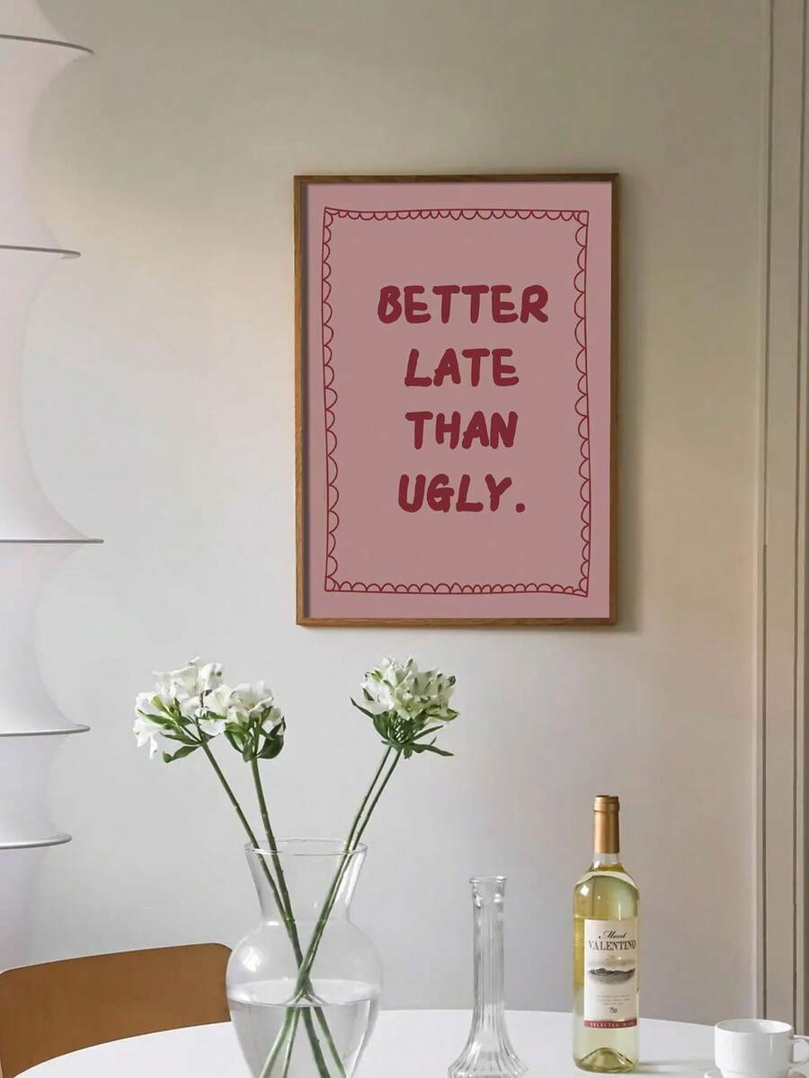 Framed BETTER LATE THAN UGLY pink typography print above dining table with flowers and wine