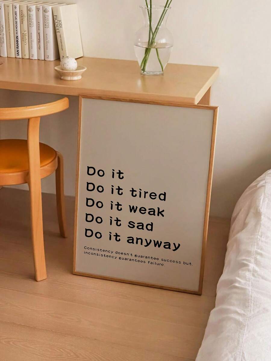 Beige consistency quote poster in wood frame leaning near desk and bed