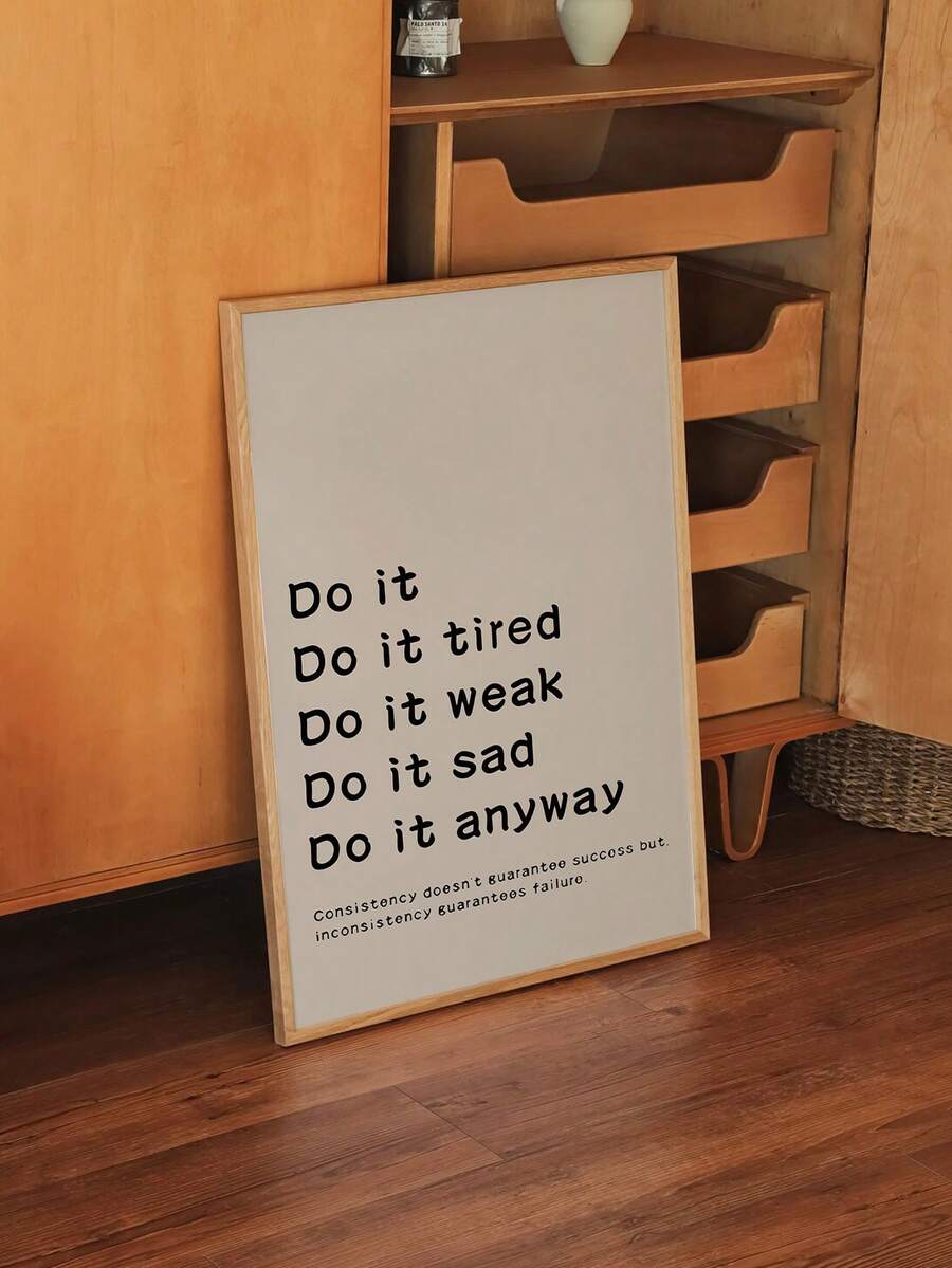 Beige consistency quote poster in wood frame leaning against wooden cabinet