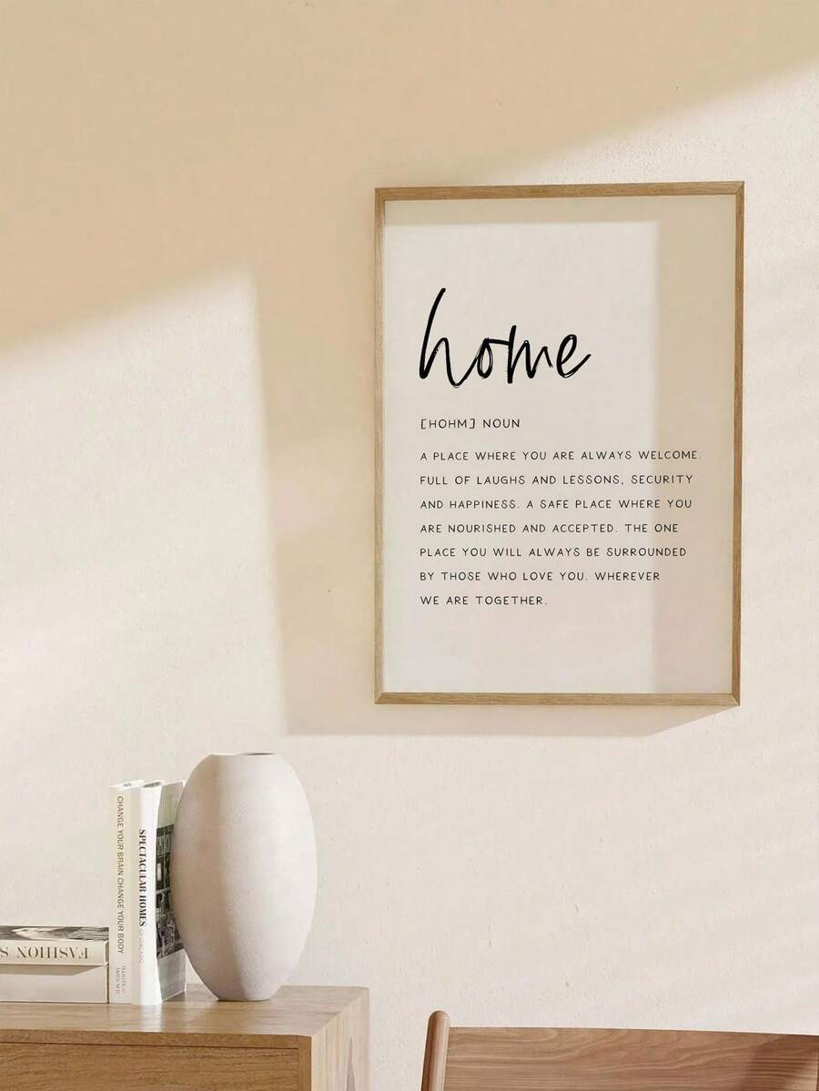 Wood framed home definition poster hanging above console table and white vase