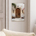 Pale wood framed doorway wall art above a neutral sofa with carved brown doors pottery palm foliage and magenta flowers