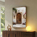 Brown wood framed architectural wall art over a dark credenza showing an ornate doorway lanterns steps pottery and flowers