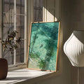 Green and turquoise abstract wall art in a light wood frame by a window