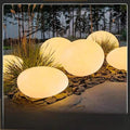 Pebble solar garden lights glowing warm in rock garden with frosted shell and black base