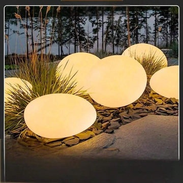 Pebble solar garden lights glowing warm in rock garden with frosted shell and black base
