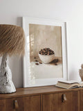 White framed coffee bean still life on wood console beside lamp and open book