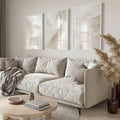 Textured neutral triptych in white frames above sectional sofa