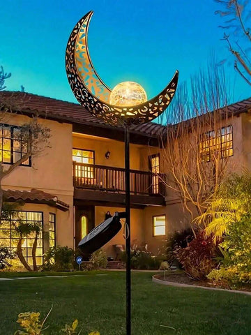 Solar moon stake light glowing in garden with warm crackle glass globe.