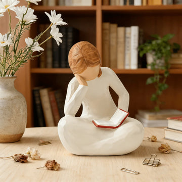 Resin reading girl figurine sitting cross-legged with open book.