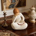 Reader figurine displayed near books, flowers, vase, and candle.