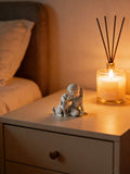 Desktop ornament of seated girl with dog beside candle and reed diffuser.