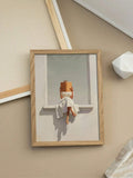 Timber framed print showing woman in white dress reading book beside minimalist decor