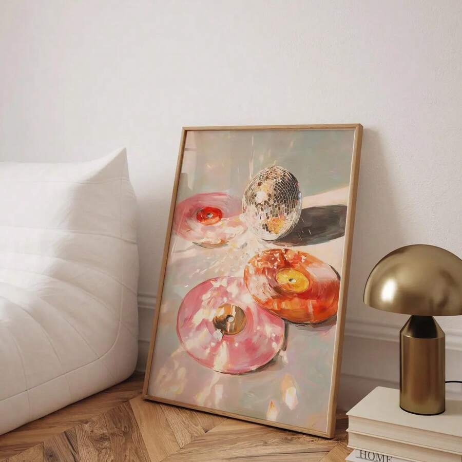 Framed portrait donut and disco ball painting leaning beside a white bed and brass lamp