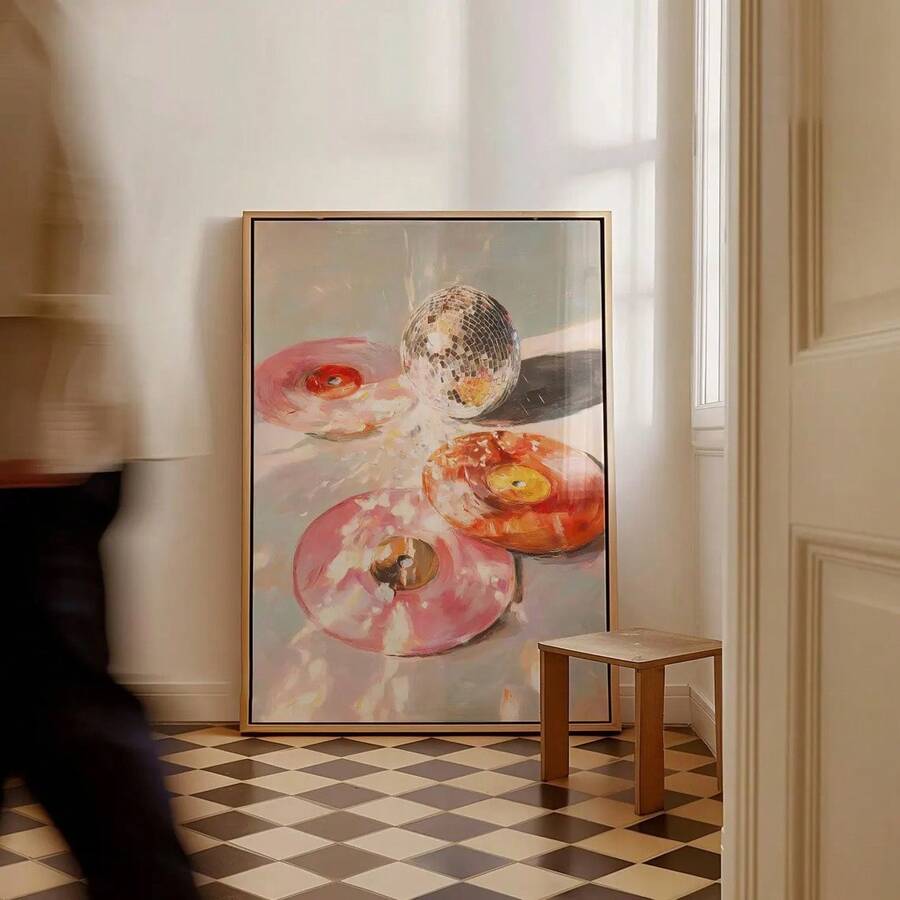 Large portrait donut and disco ball painting leaning on a cream room wall above a checkerboard floor