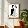 Minimalist couple and cat drawing in a pale wood frame beside green plants