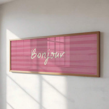 Pink framed Bonjour wall art with cream script lettering on striped blush background