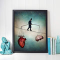 Black framed anatomical heart and brain tightrope print beside books and turquoise Buddha statue