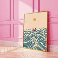 Gold-framed retro surfing girl wave poster against a pink paneled wall