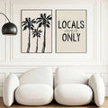 Pair of palm and coastal typography prints above pale lounge chairs