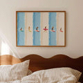 Framed surfer illustration above a bed with striped bedding and wood headboard