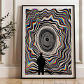 Black-framed optical illusion poster displayed beside a leafy indoor plant