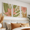 Pink floral and mustard botanical artwork in white frames above a bed with ochre pillows and a slatted headboard