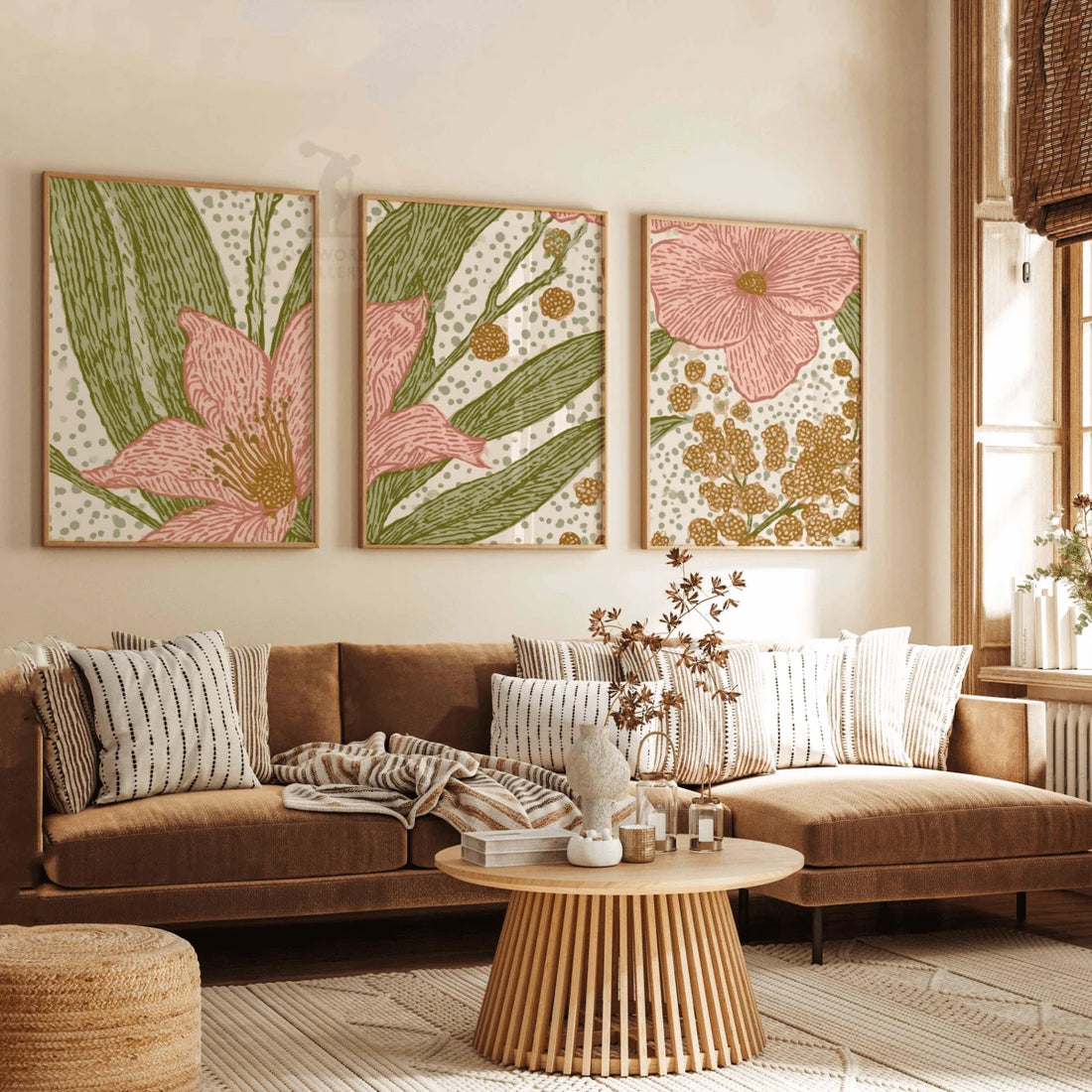 Three coordinated pink flower and mustard botanical prints in wood-toned frames leaning on a sunlit wooden floor