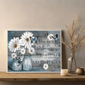 White daisy and blue butterfly canvas artwork displayed on a wooden console beside dried stems and a candle