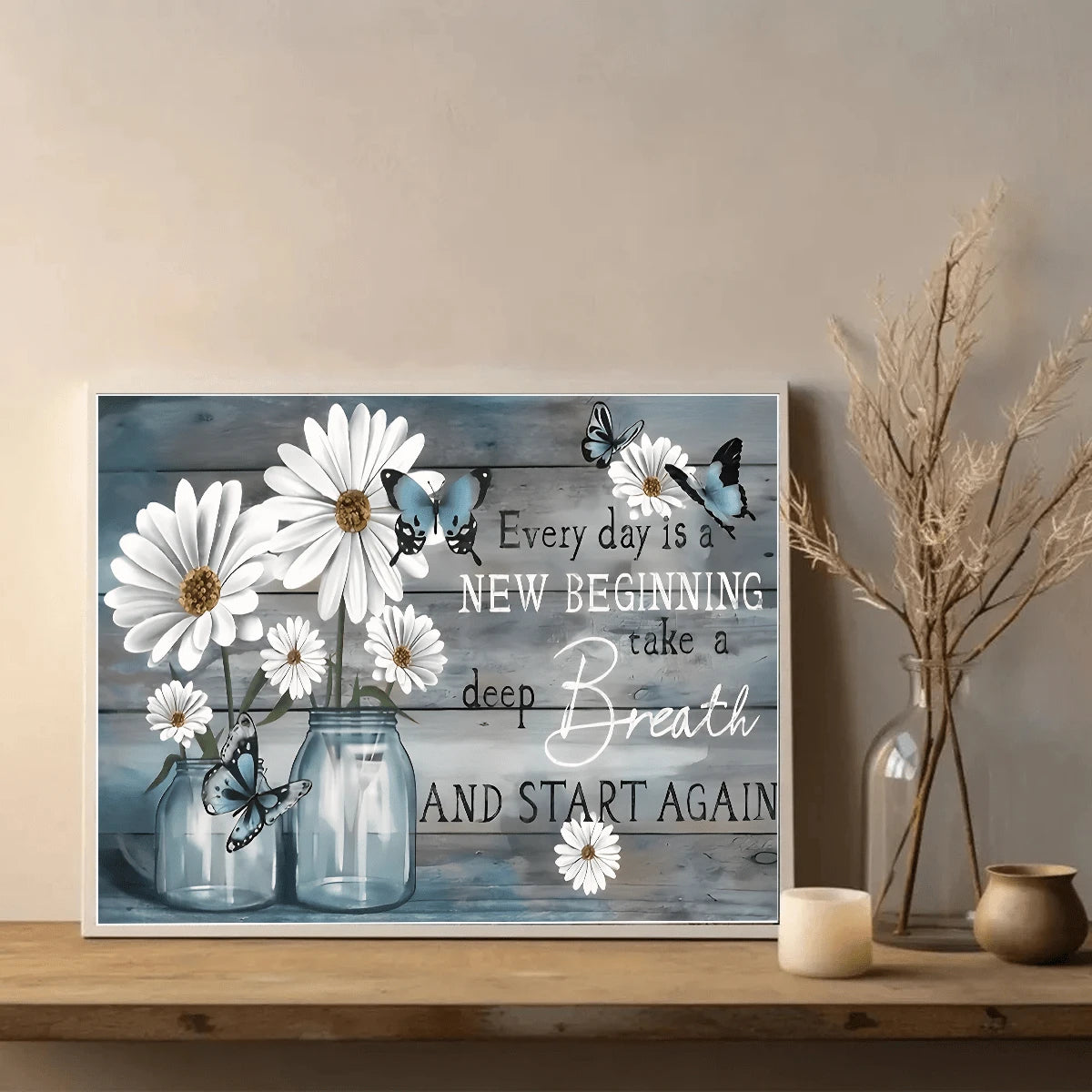 White daisy and blue butterfly canvas artwork displayed on a wooden console beside dried stems and a candle