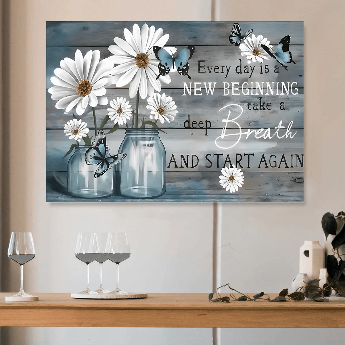 Rustic daisy and butterfly quote artwork on a blue-gray plank background above a dining console with wine glasses