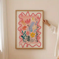 Hand holding a light-wood framed pink wildflower canvas against a pale wall