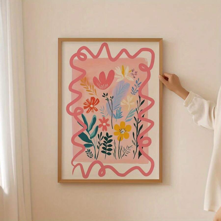 Hand holding a light-wood framed pink wildflower canvas against a pale wall