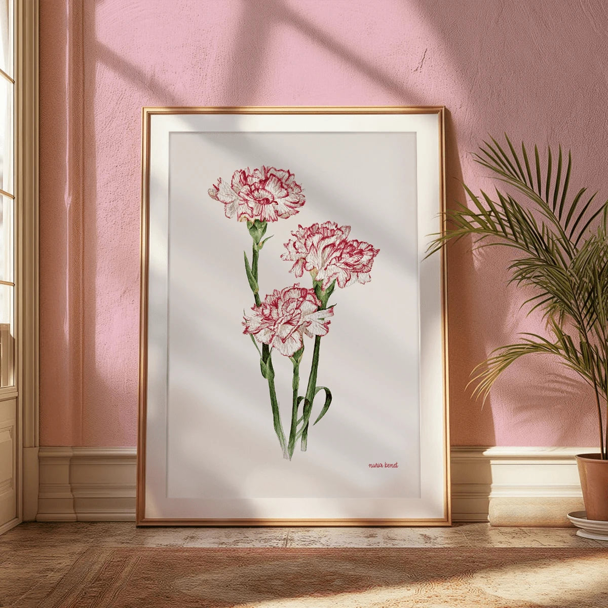 Red and white carnations on slender green stems, shown in a gold frame against a blush wall