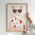 Hands holding framed cat sunglasses strawberry poster against white wall