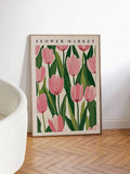 Large framed pink tulip poster leaning beside a cream lounge chair