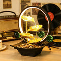 Black tabletop fountain with cascading water, pebbles, and green leaves.