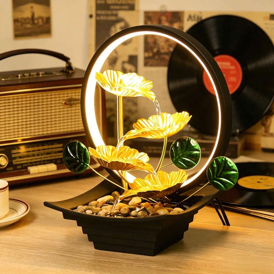 Black tabletop fountain with cascading water, pebbles, and green leaves.