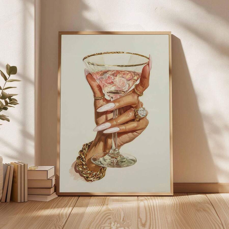 Framed luxury cocktail illustration displayed beside stacked books on a sunlit neutral wall